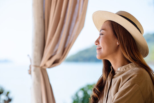 Portrait image of a beautiful young asian woman with hat looking at the beach and the sea