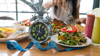 Fototapeta na wymiar Selective focus of Alarm Clock with woman hand and fork which reminding us to include delicious fresh vegetables as part of a daily healthy lifestyle diet concept