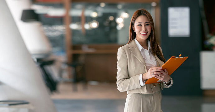 Smiling young businesswoman looking at camera while standing in the coworking space.