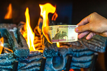 Man's hand holding a one hundred Russian rubles on fire. Currency crisis in Russia. The Russian Ruble is down. Concept of financial crisis.