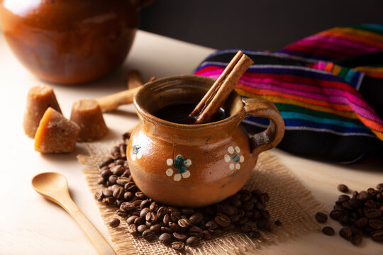 Cafe de Olla. Traditional Mexican coffee and basic ingredients for its preparation, coffee, cinnamon and piloncillo, served in a clay cup called "jarrito" on a rustic wooden surface.