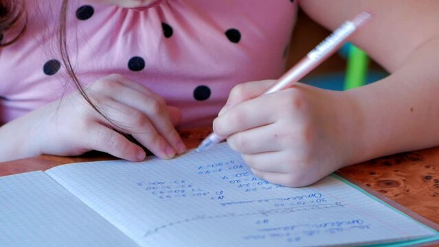 A little girl in a pink dress teaches lessons in mathematics, diligently writes numbers with her left hand. An impersonal image.