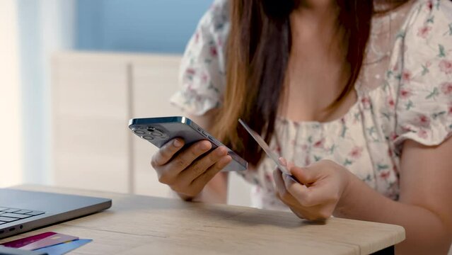 4K 50fps, A beautiful Asian woman, sitting online shopping via mobile phone, picks up a credit card and prints the card information, to pay for online purchases via mobile phone.