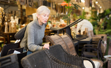 Mature caucasian woman choosing chair while shopping in furniture store.