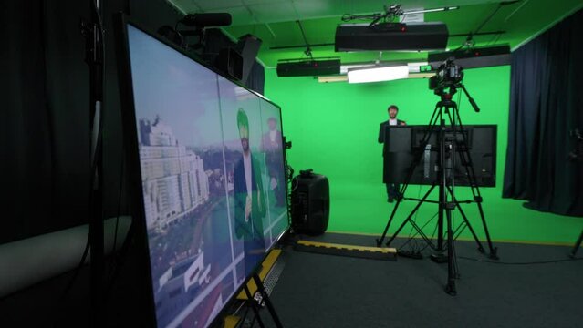 Backstage, news anchor and technical specialist at work, man reporter looks into the camera and talks, studio TV news shooting, view of the screens, live broadcast, chroma key template.