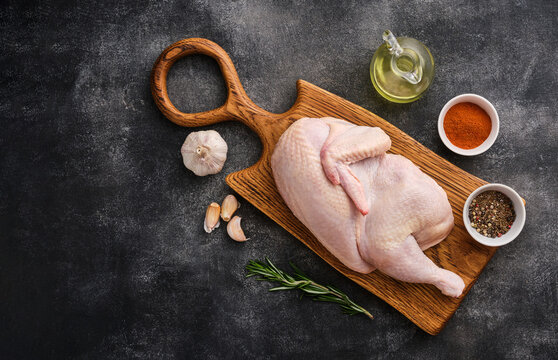 Fresh half of raw chicken with spices and seasonings on a wooden board.