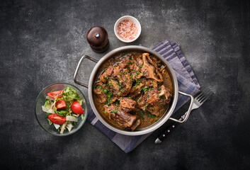 Beef oxtails stew with wine and vegetables. Dark background. Top view.