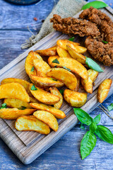 
 Crispy  deep fried   Chicken    strips ,wings and Wedges potato. Breaded  with cornflakes chicken  breast fillets  with chilly peppers and fresh   basil on wooden rustic background
