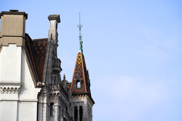 Fototapeta na wymiar Urban downtown of City of Lausanne with rooftop of building with spire and colorful tiles on a blue and cloudy spring day. Photo taken March 18th, 2022, Lausanne, Switzerland.