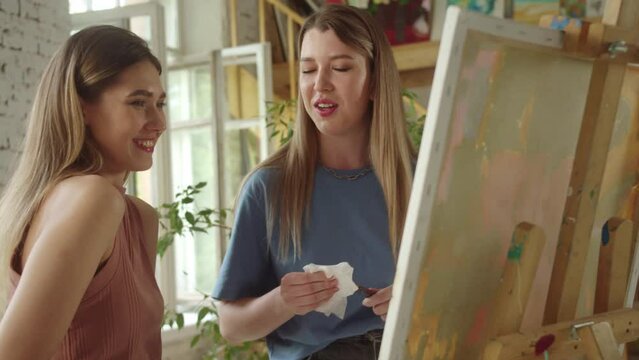 Two handsome adult girls are watching on their ready painting picture, smiling and talking, slow morion