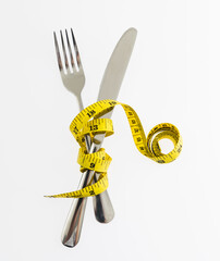 Yellow measuring tape around fork and knife on white background