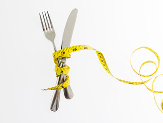 Yellow measuring tape around fork and knife on white background