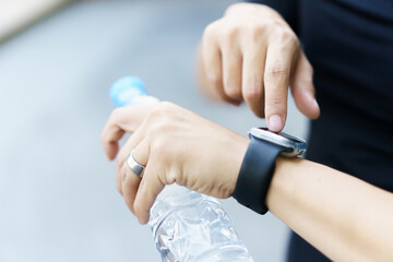 Active Asian young sportsman using a smartwatch or smart fitness band to track his outdoor workout and activities.
