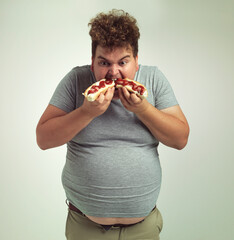 I cant get enough of these hotdogs. Studio shot of an overweight man eating two hotdogs at once.