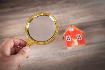 Male hand holding magnifying glass with a house model. Real estate. Inspection