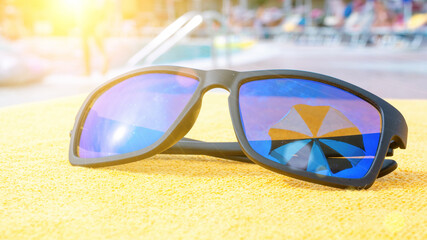 Sunglasses closeup summer background. Beach pool equipment with travel sunglasses on yellow holiday towel. Outdoor relax holiday at ocean.