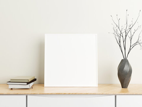 Minimalist square white poster or photo frame mockup on wood table with books and vase in a room