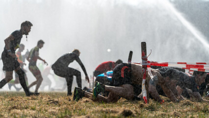 Fototapeta premium Athletes run under a crawling obstacle in water spray during obstacle course race 