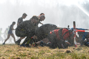 Athletes run under a crawling obstacle in water spray during obstacle course race 