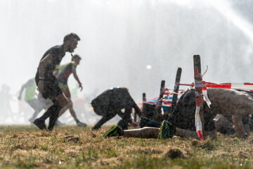 Athletes run under a crawling obstacle in water spray during obstacle course race 