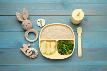 Toys, pacifier and plastic dishware with healthy baby food on light blue wooden table, flat lay