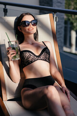 close up photo of pretty slim woman with long dark hair standing near the pool with a cocktail wearing white stylish swimwear and sunglasses. concept of luxury holiday time. free copyspace