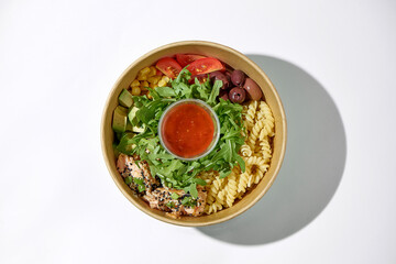 Food delivery pasta with salmon, arugula, avocado in a box on a white background.