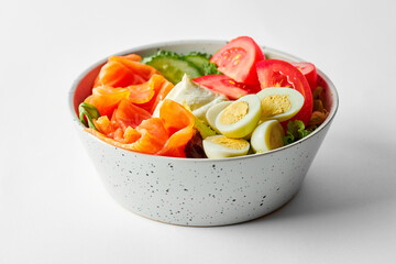 Salad with salmon, tomatoes and eggs in a bowl on a gray background. Close-up, selective focus