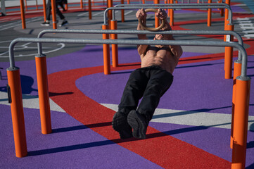 Shirtless man doing horizontal balance on parallel bars at sports ground. 