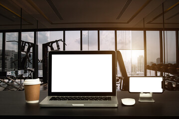 Front view of cup and laptop, smartphone, and tablet on table in Office in fitness gym in morning light.