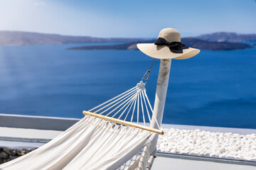 Obraz premium Summer travel concept with a hammock and a hat in front of the blue sea at Santorini island, Greece