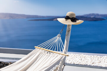 Summer travel concept with a hammock and a hat in front of the blue sea at Santorini island, Greece