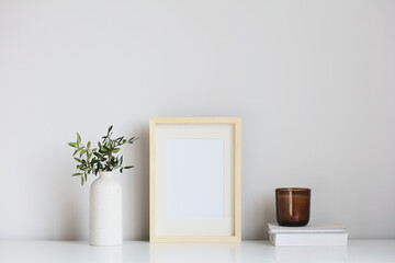 Picture frame mockup, vase of flowers, candle, book on white table. Scandinavian interior. Simple design.