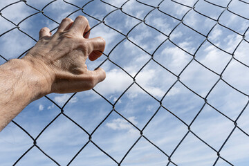 hand on a fence with the sky with clouds in the background.