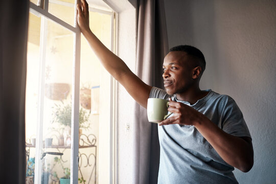 I wonder what I should do today. Cropped shot of a handsome young man standing and looking contemplative in his bedroom while enjoying a cup of coffee.