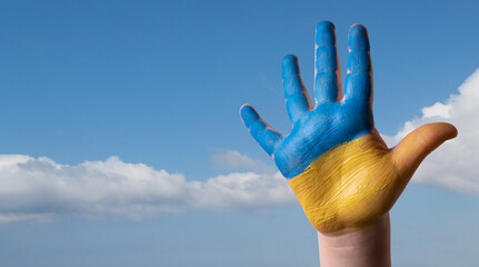 Child's hand painted in the colors of the national flag of Ukraine on blue sky background.