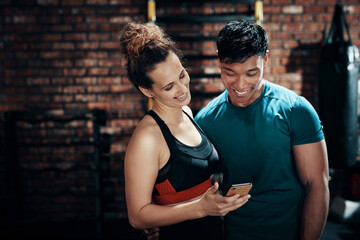 Naklejka premium Dont we just look cute here. Cropped shot of two young sportspeople using a smartphone together in a gym.