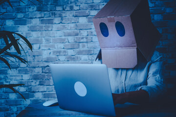 Anonymous hacker use laptop computer and connection at home wearing a box on his head to be not...