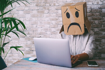 Sad people working on laptop wearing paper box on his head. Concept of stress and privacy issue on...