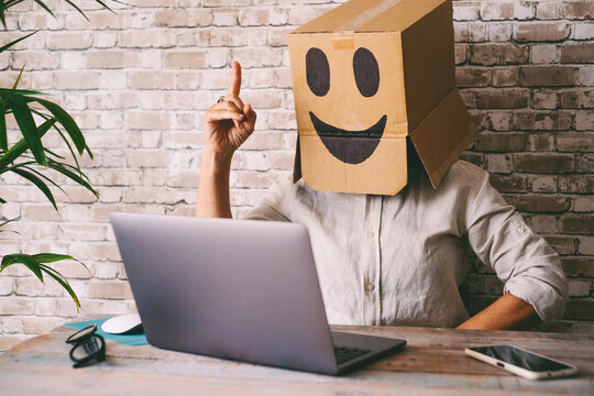 Happy and successful people working on computer wearing smile box on head. Joyful online digital anonymous worker on laptop in video call. Good news on web internet communication leisure