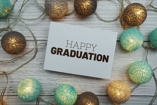 Happy Graduation Text On Paper Card With LED Cotton Balls Top View On Wooden Background