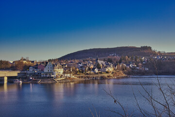 Fototapeta premium Panoramablick über den Bleilochstausee auf die Stadt Saalburg am Hang im warmen Abendlicht, Saalburg-Ebersdorf, Saale-Orla-Kreis, Thüringen, Deutschland
