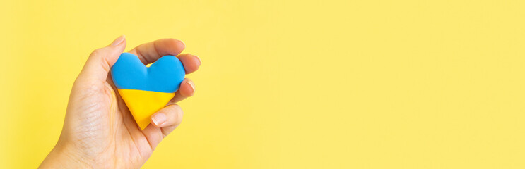 Yellow and blue heart in the colors of the flag of Ukraine in the hand of a woman. Donate for Ukraine cocnept