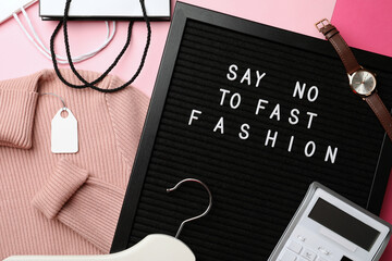 Black letter board with phrase SAY NO TO FAST FASHION, clothes, wristwatch, shopping bags, hanger...