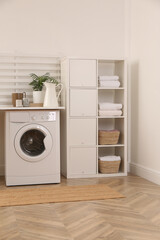 Laundry room interior with modern washing machine and shelving unit near white wall