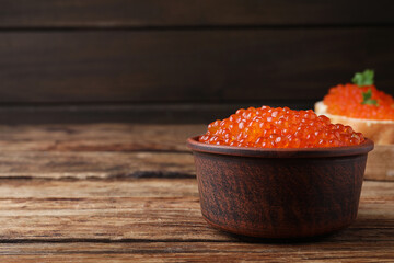 Bowl with delicious red caviar on wooden table. Space for text