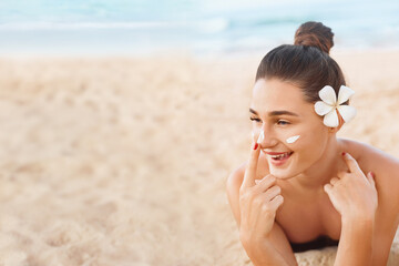 Fototapeta na wymiar Beautiful Woman In Bikini apply sun cream on Face. Woman With Suntan Lotion On Beach. Skin care. Sun protection.