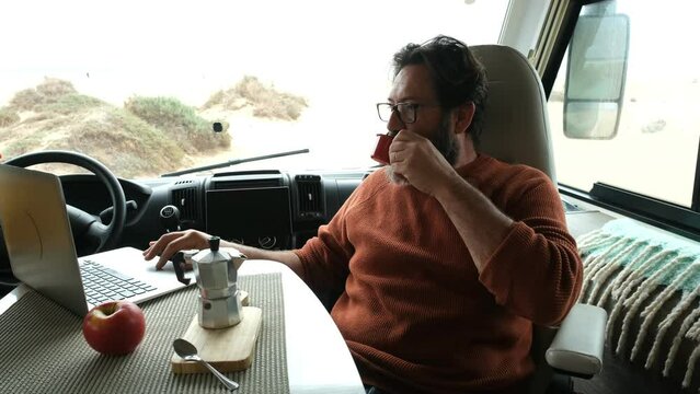 Adult man sitting inside camper van working on laptop computer comfortable. Concept of modern lifestyle and online technology job. Remote worker and digital nomad people in travel life