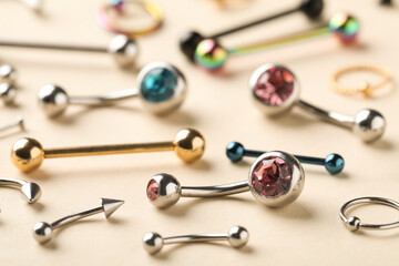 Stylish jewelry for piercing on beige background, closeup