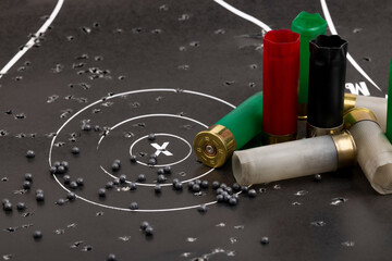 Empty fired shotgun shell and lead pellets on bull eye paper target background - obrazy, fototapety, plakaty